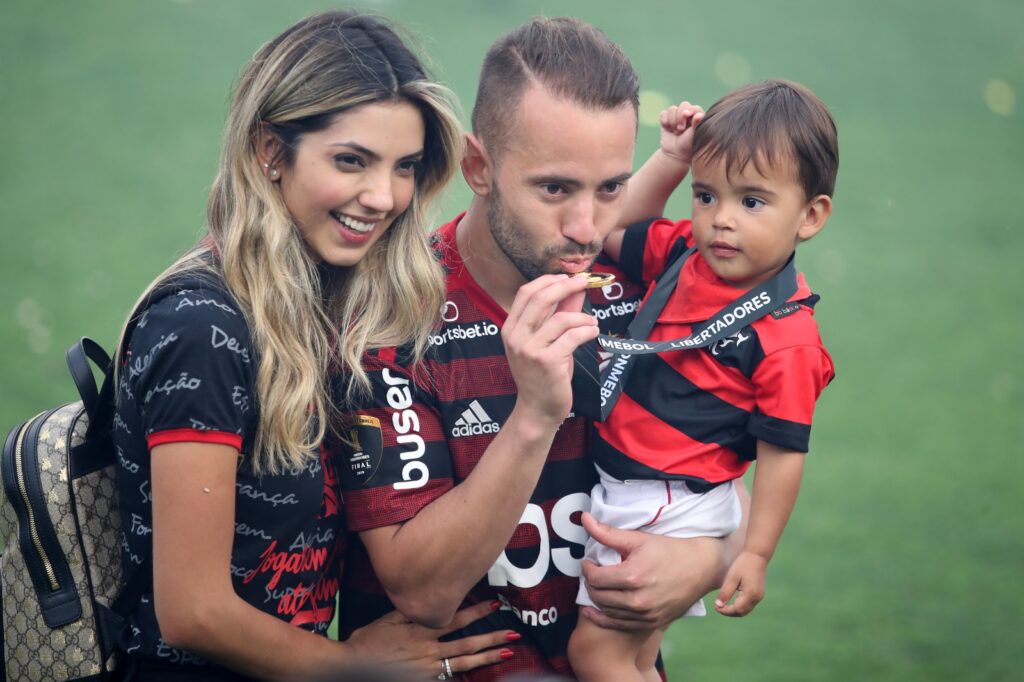 Everon Ribeiro posa beijando a medalha de campeão da Libertadores em 2019, ao lado da esposa e do filho Antônio "Totói"