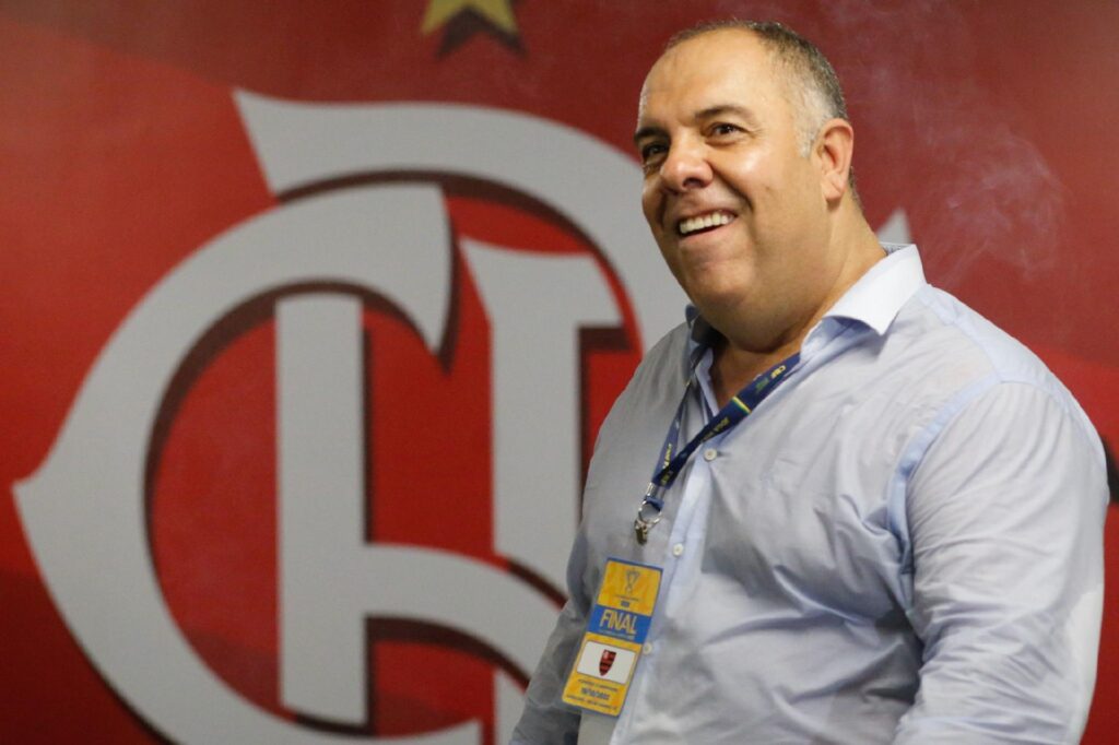 Marcos Braz sorri em frente ao escudo do Flamengo no Ninho do Urubu