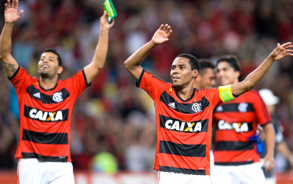 Elias em foco com os braços levantados comemorando classificação do Flamengo contra o Cruzeiro na Copa do Brasil; André Santos ao fundo e Marcelo Moreno desfocado