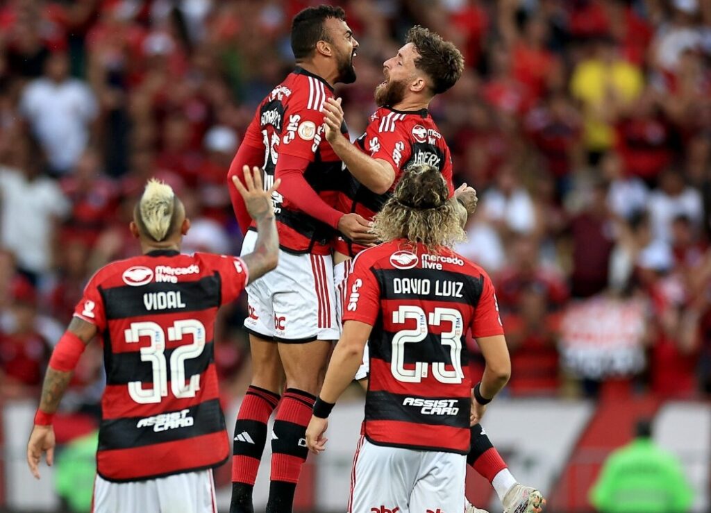 Fabrício Bruno e Léo Pereira pulam alto para comemorar gol do Flamengo; David Luiz se aproxima de dupla e aparece de costas para foto