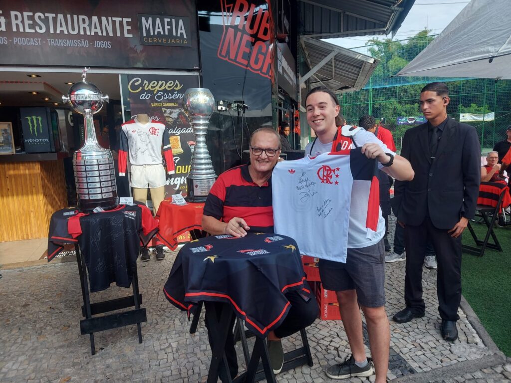 Leandro tira foto com torcedor do Flamengo após autografos em camisa retrô de 81, ao fundo, taças da Libertadores, do Mundial e camisa autografada pelo time de 81