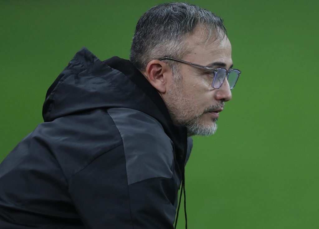 Técnico do Bolívar de óculos observando jogo contra o Flamengo na beira do campo