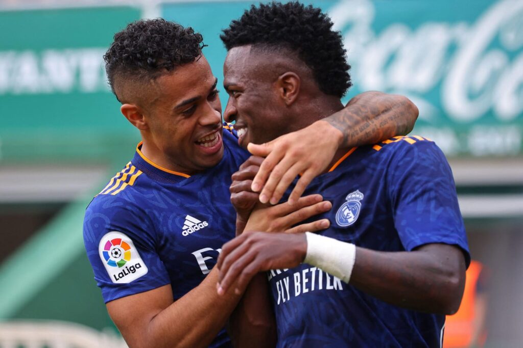 Mariano Díaz e Vinícius Júnior se abraçam sorrindo em campo pelo Real Madrid